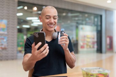 Normal ortamlarda dijital tablet bilgisayar ve salata kullanan sağlıklı yetişkin bir adam. Gıda mahkemelerinde teknoloji, beslenme ve modern yaşam tarzı arasındaki dengeyi vurgular.