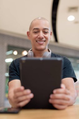 Normal ortamlarda dijital tablet bilgisayar ve salata kullanan sağlıklı yetişkin bir adam. Gıda mahkemelerinde teknoloji, beslenme ve modern yaşam tarzı arasındaki dengeyi vurgular.