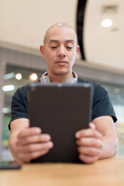 Normal ortamlarda dijital tablet bilgisayar ve salata kullanan sağlıklı yetişkin bir adam. Gıda mahkemelerinde teknoloji, beslenme ve modern yaşam tarzı arasındaki dengeyi vurgular.