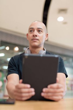 Normal ortamlarda dijital tablet bilgisayar ve salata kullanan sağlıklı yetişkin bir adam. Gıda mahkemelerinde teknoloji, beslenme ve modern yaşam tarzı arasındaki dengeyi vurgular.