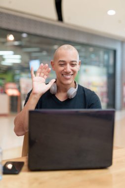 Siyah tişörtlü kel adam alışveriş merkezinde tek başına dizüstü bilgisayar kullanıyor. Toplum içinde odaklanmış dijital çalışma ve üretkenlik teması. Gerçek yaşam tarzı anı, tarafsız ve modern..