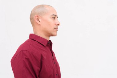 Burgonya gömlekli, beyaz arka planda duran kendine güvenen kel, yetişkin bir adam. Stüdyo portre tarzı, temiz, minimal, profesyonel görünüm..