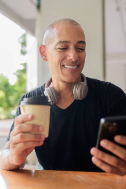 Kel adam yazın mutlu bir şekilde gülümserken dışarıda cep telefonu kullanırken oturuyor ve gülümsüyor.