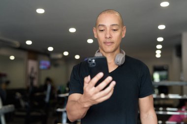 Spor salonunda antrenman yapan kel, İspanyol bir adam. Kaslı erkek, içeride özgüvenle egzersiz yapıyor, siyah gömlek ve kulaklık takıyor. Sağlıklı yaşam tarzı, güç ve sağlığa odaklanma..