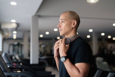 Spor salonunda antrenman yapan kel, İspanyol bir adam. Kaslı erkek, içeride özgüvenle egzersiz yapıyor, siyah gömlek ve kulaklık takıyor. Sağlıklı yaşam tarzı, güç ve sağlığa odaklanma..