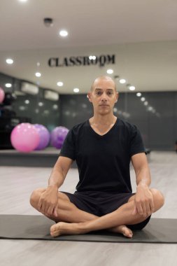 Spor salonunda antrenman yapan kel, İspanyol bir adam. Kaslı erkek, evde kendine güvenerek egzersiz yapıyor, yoga yaparken siyah gömlek giyiyor. Sağlıklı yaşam tarzı, yoga ve sağlık odaklanması.