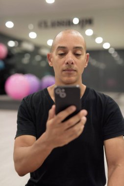 Spor salonunda antrenman yapan kel, İspanyol bir adam. Kaslı erkek, içeride özgüvenle egzersiz yapıyor, siyah gömlek giyiyor. Sağlıklı yaşam tarzı, güç ve sağlığa odaklanma..