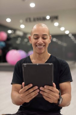 Spor salonunda antrenman yapan kel, İspanyol bir adam. Kaslı erkek, dijital tablet bilgisayar kullanıyor, kendine güveni var, siyah gömlek giyiyor. Sağlıklı yaşam tarzı, güç ve sağlığa odaklanma..