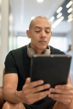 Spor salonunda spor yaptıktan sonra sporcu olan İspanyol kel adam rahatlıyor ve açık sözlü dijital tablet bilgisayar kullanıyor.