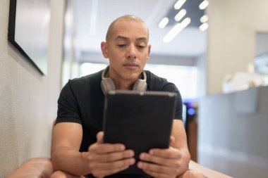 Spor salonunda spor yaptıktan sonra sporcu olan İspanyol kel adam rahatlıyor ve açık sözlü dijital tablet bilgisayar kullanıyor.