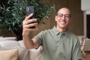 Gözlüklü Latin yetişkin adam otel lobisinde ya da bar salonunda otururken telefon kullanıyor. Modern dijital yaşam tarzı, günlük iş ortamı, seyahat ortamında iletişim ve bağlantı.