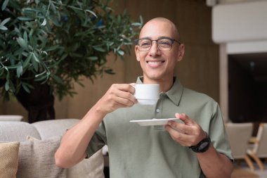 Otel kafesinde ya da dinlenme odasında oturan olgun kel bir adam elinde kahve ya da çay tutuyordu. Konukseverliği yansıtır, sakin bir tatil, zarif bar dekorasyonu, günlük iş ve sağlık yaşam tarzını yansıtır..