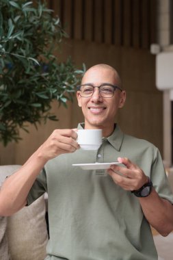 Otel kafesinde ya da dinlenme odasında oturan olgun kel bir adam elinde kahve ya da çay tutuyordu. Konukseverliği yansıtır, sakin bir tatil, zarif bar dekorasyonu, günlük iş ve sağlık yaşam tarzını yansıtır..