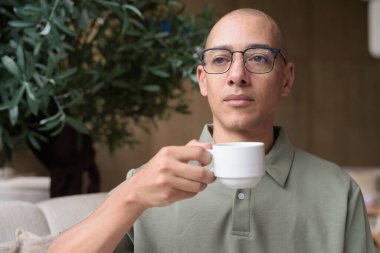 Otel kafesinde ya da dinlenme odasında oturan olgun kel bir adam elinde kahve ya da çay tutuyordu. Konukseverliği yansıtır, sakin bir tatil, zarif bar dekorasyonu, günlük iş ve sağlık yaşam tarzını yansıtır..