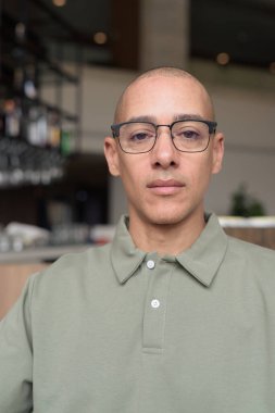 40 'lı yaşlarda Latin bir adam otel kafesinde ya da barda modern iç mimari ile poz veriyor. Vesikalık, zarif iş-gündelik görünüş, rahat tavır, güven ve yakışıklı olgun erkeklik üzerine odaklanmış..