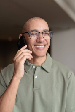 Gözlüklü Latin yetişkin adam otel lobisinde ya da bar salonunda otururken telefon kullanıyor. Modern dijital yaşam tarzı, günlük iş ortamı, seyahat ortamında iletişim ve bağlantı.