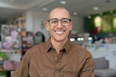 40 'lı yaşlarda kel bir adam kafeteryada oturuyor, günlük gömlek ve gözlük takıyor. Kendinden emin ve mutlu bir ifade. Kentsel yaşam tarzı, modern adam, rahat ortamda yetişkin portresi.