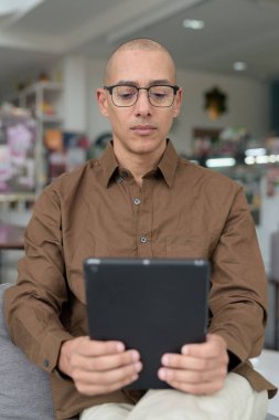 Rahat bir kafede otururken 40 'lı yaşlarındaki kel bir adamın tablet tabletini kullanması. Gözlük takıyor ve sıradan bir gömlek giyiyor. Teknoloji, dijital alışkanlıklar ve eğlence yaşam tarzı teması.