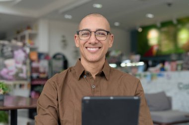 Rahat bir kafede otururken 40 'lı yaşlarındaki kel bir adamın tablet tabletini kullanması. Gözlük takıyor ve sıradan bir gömlek giyiyor. Teknoloji, dijital alışkanlıklar ve eğlence yaşam tarzı teması.