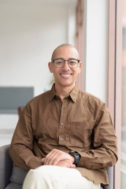 40 'lı yaşlarda kel bir adam kafeteryada oturuyor, günlük gömlek ve gözlük takıyor. Kendinden emin ve mutlu bir ifade. Kentsel yaşam tarzı, modern adam, rahat ortamda yetişkin portresi.