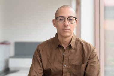 40 'lı yaşlarda kel bir adam kafeteryada oturuyor, günlük gömlek ve gözlük takıyor. Kendinden emin ve mutlu bir ifade. Kentsel yaşam tarzı, modern adam, rahat ortamda yetişkin portresi.