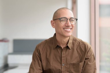 40 'lı yaşlarda kel bir adam kafeteryada oturuyor, günlük gömlek ve gözlük takıyor. Kendinden emin ve mutlu bir ifade. Kentsel yaşam tarzı, modern adam, rahat ortamda yetişkin portresi.