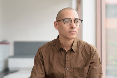 40 'lı yaşlarda kel bir adam kafeteryada oturuyor, günlük gömlek ve gözlük takıyor. Kendinden emin ve mutlu bir ifade. Kentsel yaşam tarzı, modern adam, rahat ortamda yetişkin portresi.