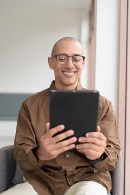 Rahat bir kafede otururken 40 'lı yaşlarındaki kel bir adamın tablet tabletini kullanması. Gözlük takıyor ve sıradan bir gömlek giyiyor. Teknoloji, dijital alışkanlıklar ve eğlence yaşam tarzı teması.