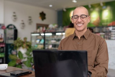 Kapalı kafede dizüstü bilgisayar kullanan, gözlük takan ve gömleğini ilikleyen olgun bir İspanyol. Kendine güvenen ve odaklanmış ifade. Şehir ortamında uzak çalışma, serbest çalışma, teknoloji meraklısı yaşam tarzı konsepti.