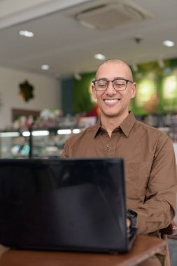 Kapalı kafede dizüstü bilgisayar kullanan, gözlük takan ve gömleğini ilikleyen olgun bir İspanyol. Kendine güvenen ve odaklanmış ifade. Şehir ortamında uzak çalışma, serbest çalışma, teknoloji meraklısı yaşam tarzı konsepti.