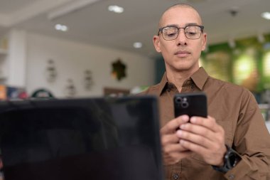 Kapalı kafede dizüstü bilgisayar kullanan, gözlük takan ve gömleğini ilikleyen olgun bir İspanyol. Kendine güvenen ve odaklanmış ifade. Şehir ortamında uzak çalışma, serbest çalışma, teknoloji meraklısı yaşam tarzı konsepti.