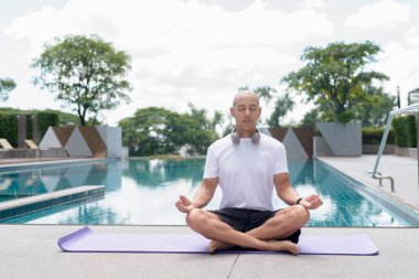Meditasyon yapan Latin kel adam havuz başında poz veriyor. Sakin ve huzurlu bir an yoga, farkındalık, manevi odaklanma ve açık havada sağlıklı yaz yaşam tarzını yansıtıyor..
