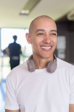 Modern spor salonunda kendine güvenen kel Latin bir adam. Sağlık, eğitim disiplini ve ev ortamında güçlü ve sağlıklı bir yaşam tarzının portresi..