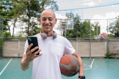 Spor giyim bölümündeki kel adam basketbol sahasında akıllı telefon kullanıyor. Kentsel fitness ve sağlıklı yaşam tarzı konsepti modern teknoloji ile atletik eğitimi harmanlıyor.
