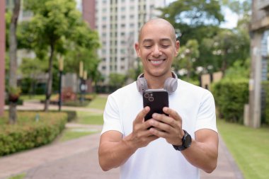 Parkta ya da şehir merkezinde yürürken telefonu kullanan kel bir İspanyol. Modern dijital yaşam tarzını, sağlıklı hareket alışkanlıklarını ve açık hava dengesini temsil eder..