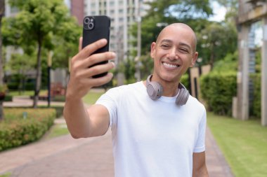 Parkta ya da şehir merkezinde yürürken telefonu kullanan kel bir İspanyol. Modern dijital yaşam tarzını, sağlıklı hareket alışkanlıklarını ve açık hava dengesini temsil eder..