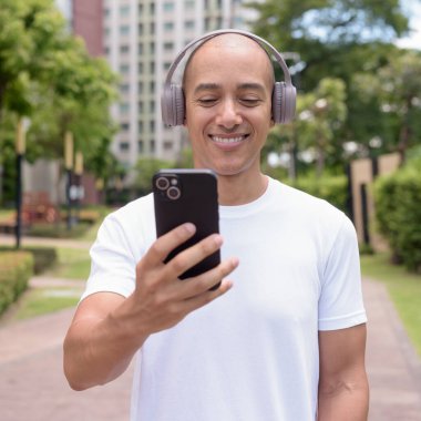 Parkta ya da şehir merkezinde yürürken telefonu kullanan kel bir İspanyol. Modern dijital yaşam tarzını, sağlıklı hareket alışkanlıklarını ve açık hava dengesini temsil eder..