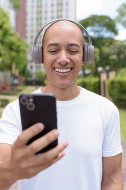 Parkta ya da şehir merkezinde yürürken telefonu kullanan kel bir İspanyol. Modern dijital yaşam tarzını, sağlıklı hareket alışkanlıklarını ve açık hava dengesini temsil eder..