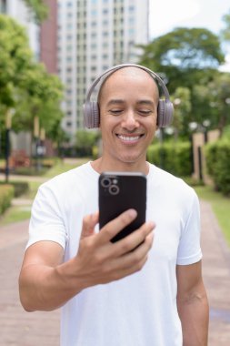 Parkta ya da şehir merkezinde yürürken telefonu kullanan kel bir İspanyol. Modern dijital yaşam tarzını, sağlıklı hareket alışkanlıklarını ve açık hava dengesini temsil eder..