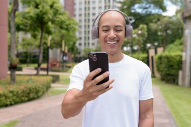 Parkta ya da şehir merkezinde yürürken telefonu kullanan kel bir İspanyol. Modern dijital yaşam tarzını, sağlıklı hareket alışkanlıklarını ve açık hava dengesini temsil eder..