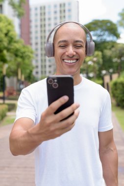 Parkta ya da şehir merkezinde yürürken telefonu kullanan kel bir İspanyol. Modern dijital yaşam tarzını, sağlıklı hareket alışkanlıklarını ve açık hava dengesini temsil eder..