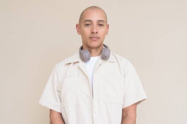 Boynuna bej gömlek ve kulaklık takmış, bej arka planda duran kel İspanyol adamın portresi..