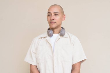 Boynuna bej gömlek ve kulaklık takmış, bej arka planda duran kel İspanyol adamın portresi..