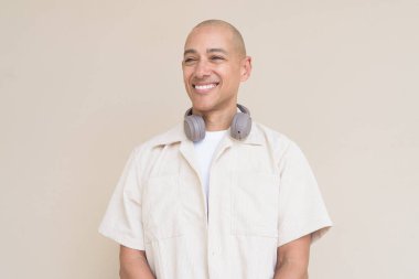 Boynuna bej gömlek ve kulaklık takmış, bej arka planda duran kel İspanyol adamın portresi..