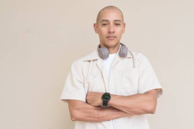 Boynuna bej gömlek ve kulaklık takmış, bej arka planda duran kel İspanyol adamın portresi..