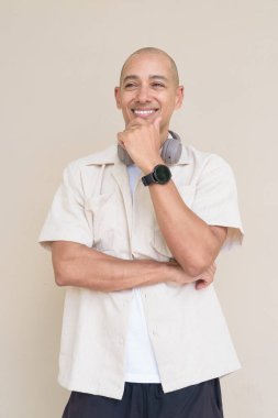 Boynuna bej gömlek ve kulaklık takmış, bej arka planda duran kel İspanyol adamın portresi..