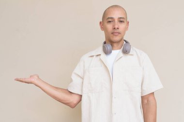 Boynuna bej gömlek ve kulaklık takmış, bej arka planda duran kel İspanyol adamın portresi..