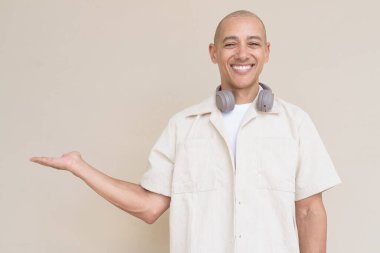 Boynuna bej gömlek ve kulaklık takmış, bej arka planda duran kel İspanyol adamın portresi..