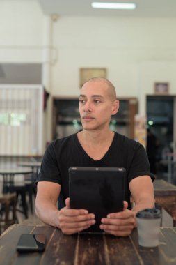 Siyah tişört giyen kel Latin bir adamın portresi, basit bir açık kahve dükkanında tek başına oturuyor.