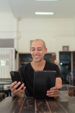 Siyah tişört giyen kel Latin bir adamın portresi, basit bir açık kahve dükkanında tek başına oturuyor.